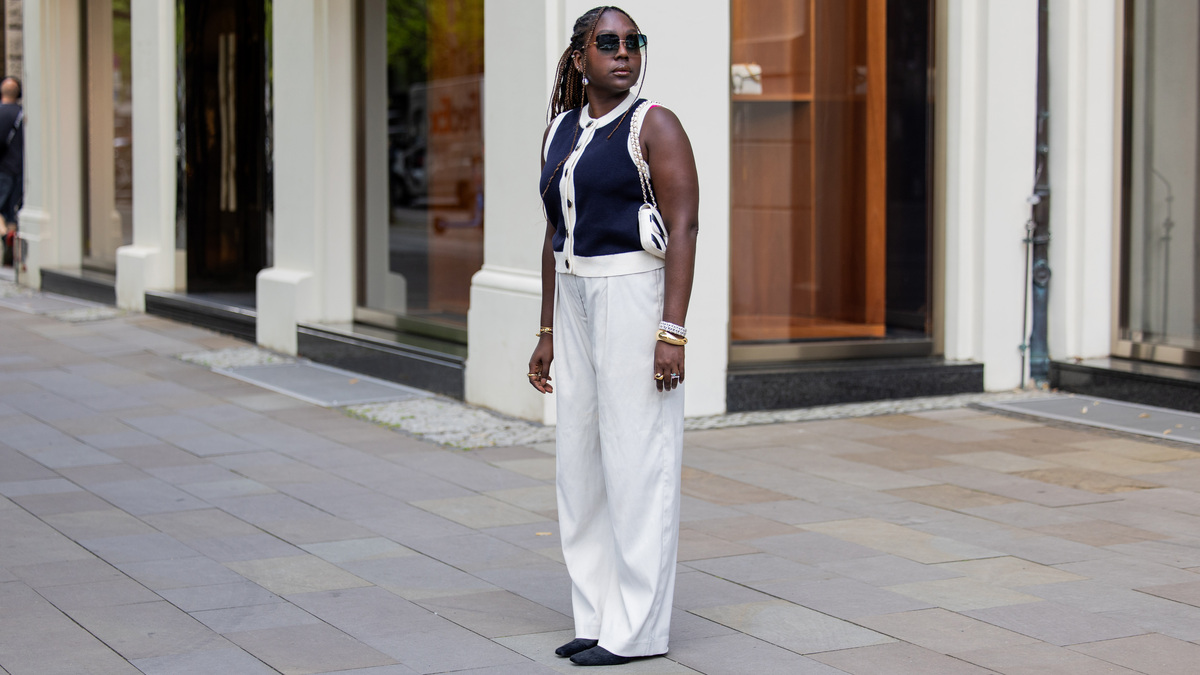 BERLIN, GERMANY - JULY 02: Lois Opoku wears navy cardigan sleeveless vest Sezane, white pants Monki, heels H&M Studio, sunglasses Kate Spade, black white Chanel bag, bracelet during the Berlin Fashion Week Spring/Summer 2026 at  on July 02, 2026 in Berlin, Germany. (Photo by Christian Vierig/Getty Images)