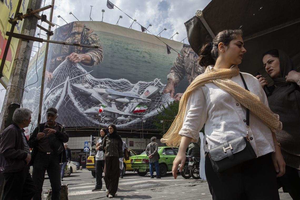 People pass near a billboard depicting American aircraft in a net in Enghelab Square in Tehran, on Monday, April 20, 2026. Despite sending mixed signals in recent days, both the United States and Iran gave clearer indications on Monday that they were planning to send negotiators to peace talks in Pakistan this week. (Arash Khamooshi/The New York Times)