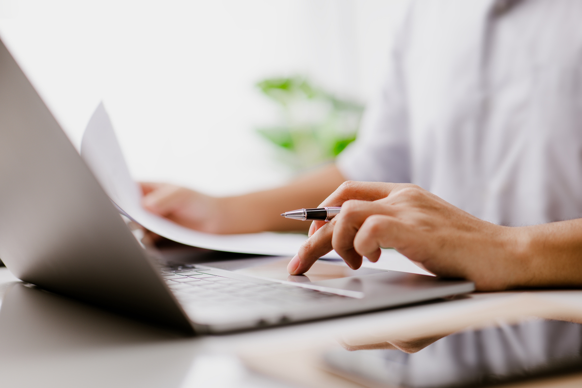  A stock image shows a hand typing on a laptop keyboard, while reading a business document. 