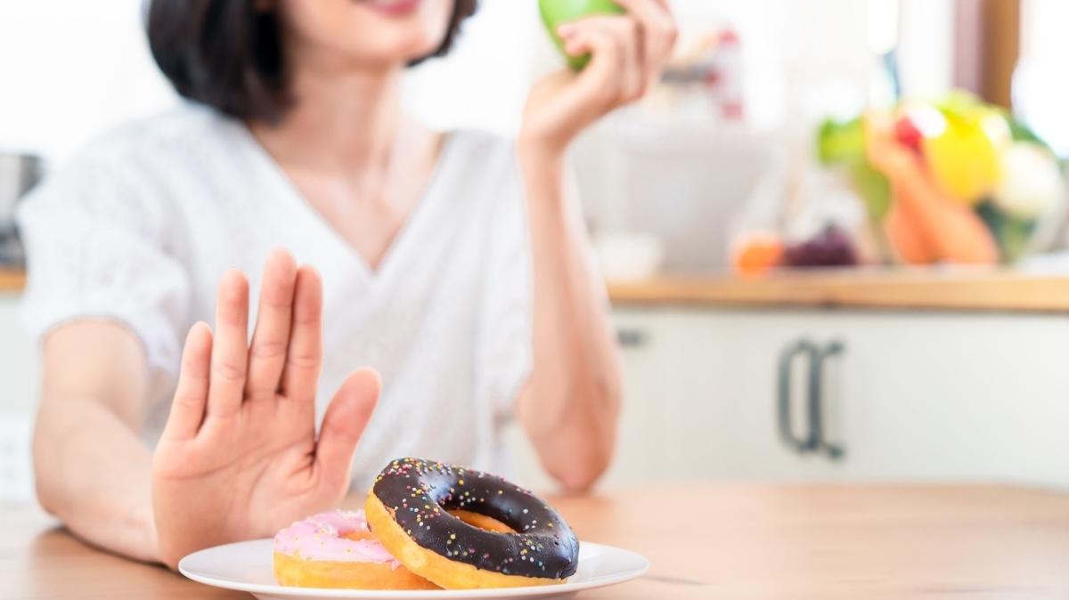Asian woman sitting in kitchen. Lady hold fresh apple with high vitamin and mineral at the same time girl refuse junk food. Good nutrition food from vegetable and fruit. Natural diet healthy concept.