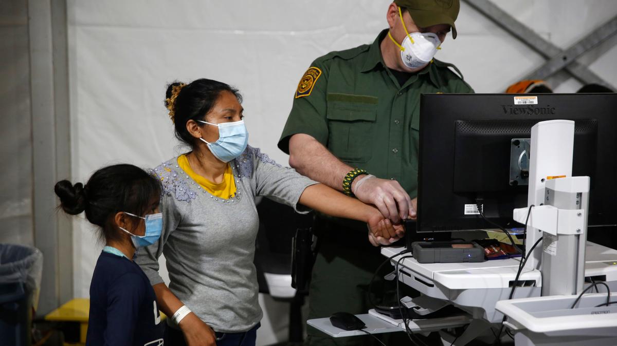 Un agente de frontera toma las huellas dactilares de una mujer inmigrante y su hija en el principal centro de detención para menores no acompañados del Departamento de Seguridad Nacional, en el Valle del Río Grande, en Donna Texas, el 30 de marzo de 2021.