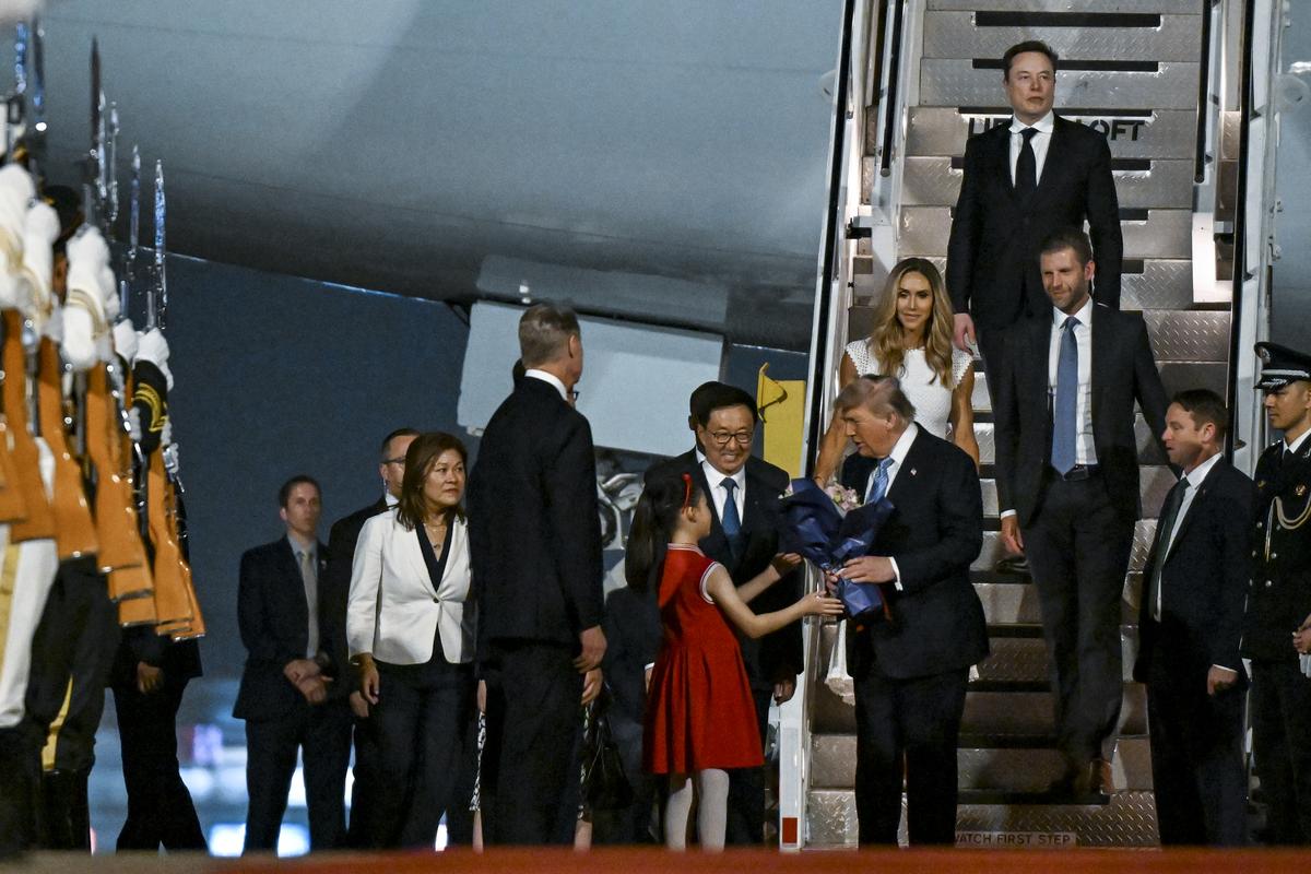President Donald Trump receives flowers as he arrives at Beijing Capital International Airport in Beijing, China, on Wednesday, May 13, 2026, for a two-day summit with China's leader, Xi Jinping. Behind Trump are Eric and Lara Trump and Elon Musk, top. (Kenny Holston/The New York Times)