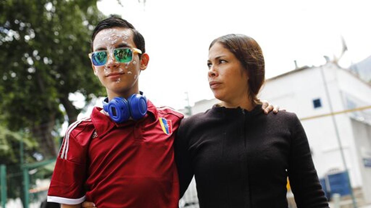Foto de archivo. Rufo Chacón, quien utiliza gafas reflectantes tras perder la vista debido a perdigones disparados por la policía durante una protesta, y su madre, Adriana Parada, son recibidos por numerosos reporteros a la llegada de ambos a las oficinas de Foro Penal, una organización venezolana de derechos humanos, en Caracas, el viernes 19 de julio de 2019.
