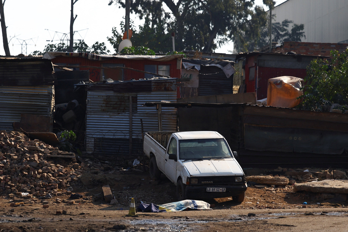 A body lies covered next to a vehicle after, according to the police, gunmen opened fire at an informal settlement in Johannesburg, South Africa,  June 10, 2026. REUTERS/Siphiwe Sibeko