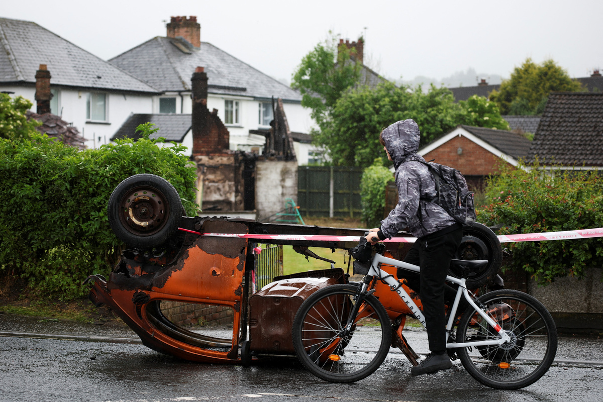 A person cycles past a burnt car in front of a burnt derelict house at Antrim Road, in the aftermath of anti-immigrant protests following a knife attack on June 8, which left a man seriously injured and prompted police to declare a critical incident, in Belfast, Northern Ireland, June 11, 2026. REUTERS/Isabel Infantes