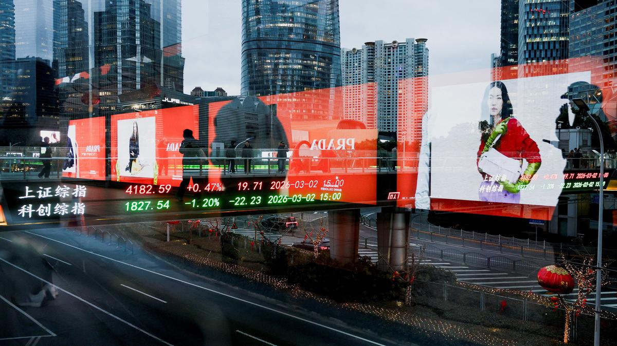 FILE PHOTO: An electronic board shows Shanghai stock indices as people walk on a pedestrian bridge in the Lujiazui financial district in Shanghai, China, March 2, 2026. Picture taken through glass. REUTERS/Go Nakamura/ File Photo