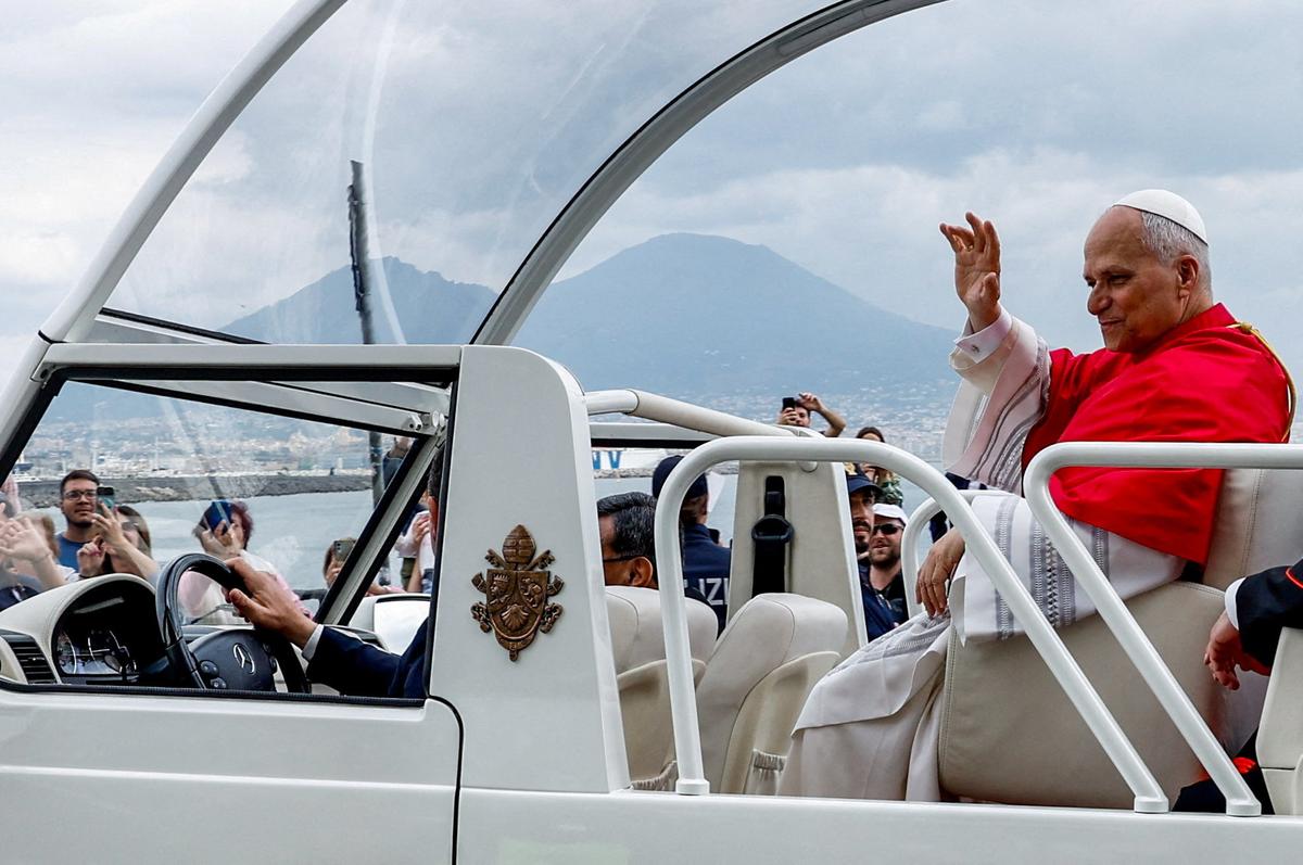 Pope Leo XIV waves to the faithful while travelling in the popemobile along the waterfront with Mount Vesuvius in the background, on the day of the first anniversary of his election in Naples, Italy, May 8, 2026. REUTERS/Remo Casilli