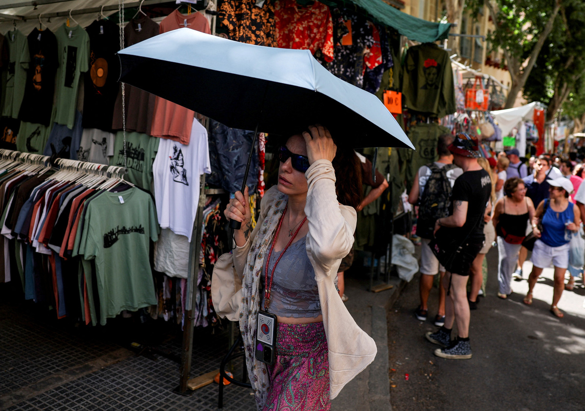 A woman walks with an umbrella, as tourists and residents shop at El Rastro flea market during a hot summer day in central Madrid, Spain June 21, 2026.  REUTERS/Mohammed Salem