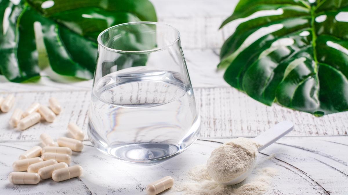 Glass of water, collagen powder and pills on white wooden table. Healthy lifestyle concept. Copy space