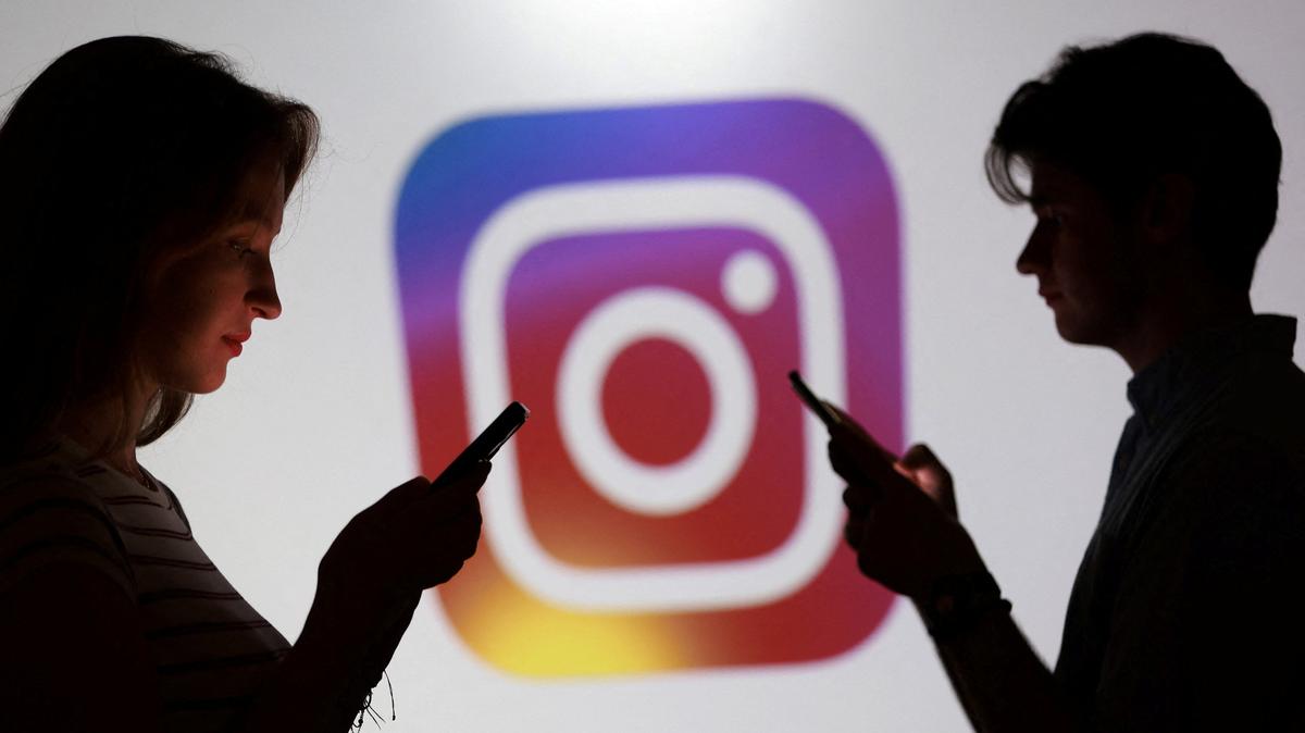 Teenagers pose for a photo while holding smartphones in front of a Instagram logo in this illustration taken September 11, 2025. REUTERS/Dado Ruvic/Illustration