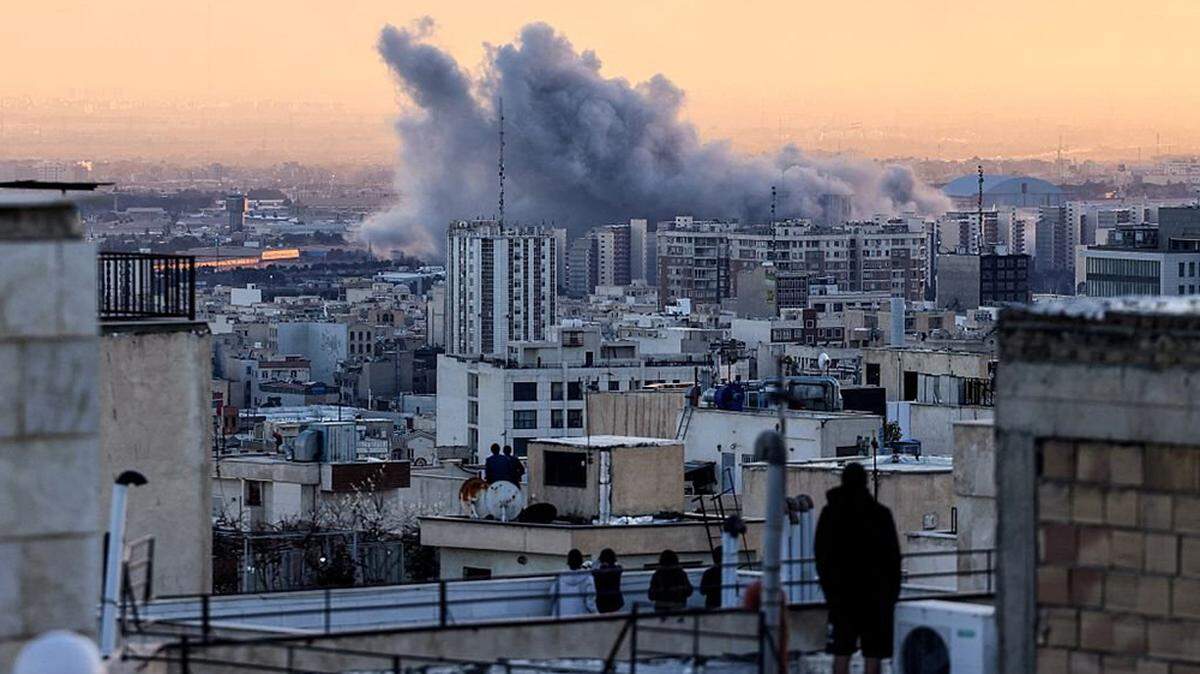 A person stands on the roof of a building looking at a plume of smoke rises after a strike on the Iranian capital of Tehran on Tuesday, March 3, 2026.