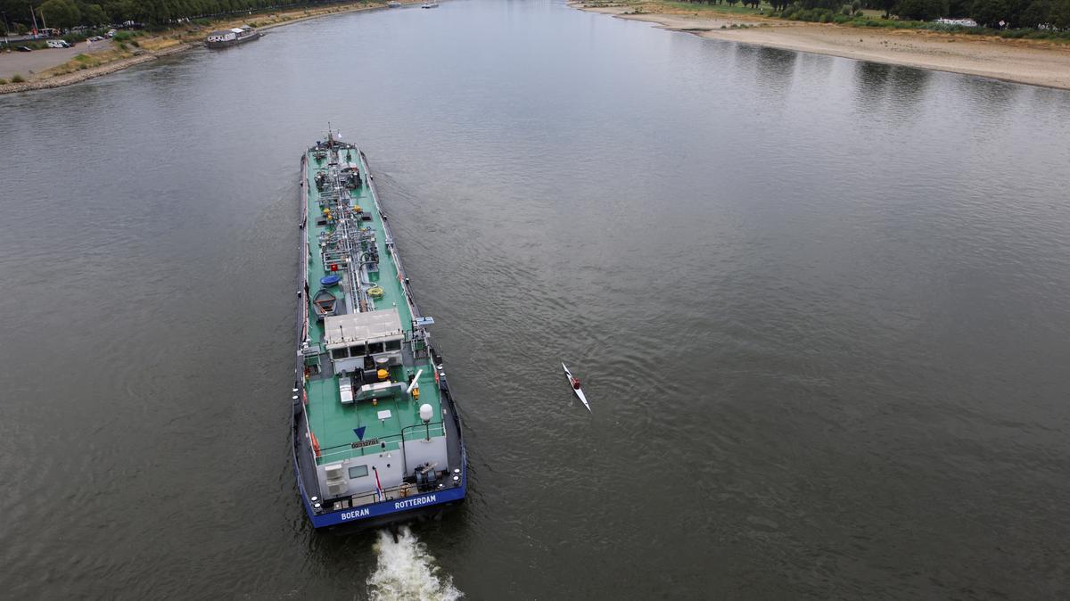 A canoer paddles next to a cargo ship at low water levels in the Rhine river in Cologne, Germany, August 15, 2022. REUTERS/Thilo Schmuelgen