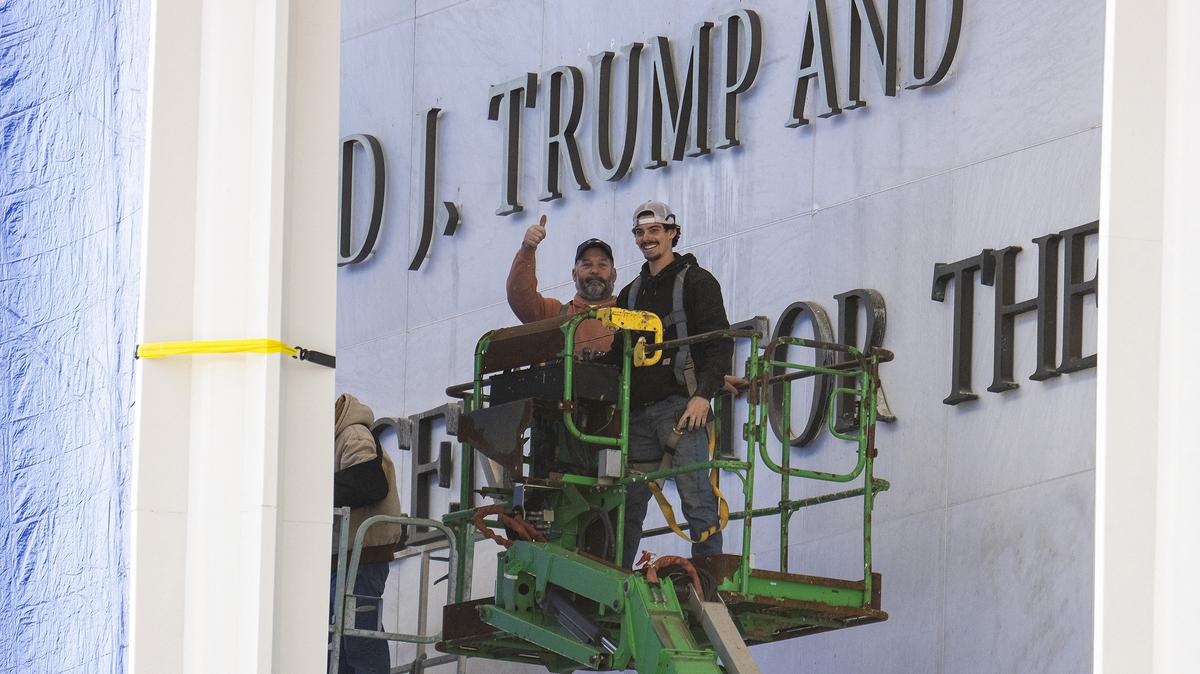Workers react to the media as they come down off a scissor lift after updating signage outside the The John F. Kennedy Memorial Center for the Performing Arts after the building was renamed in honor of President Donald Trump on Dec. 19, 2025, in Washington, D.C. (Jim Watson/AFP via Getty Images/TNS)