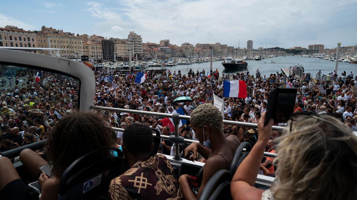 Turistas en un autobús en Marsella, en el sur de Francia, ven una protesta en contra de la exigencia de tener la prueba de vacunación contra el COVID-19, el sábado 7 de agosto de 2021.