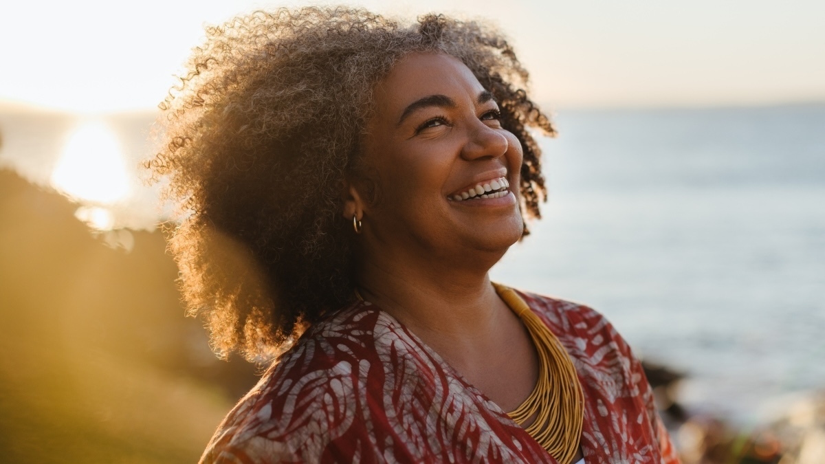 Smiling mature woman enjoying a moment of healthy living by the sea at sunset, radiating happiness and contentment.