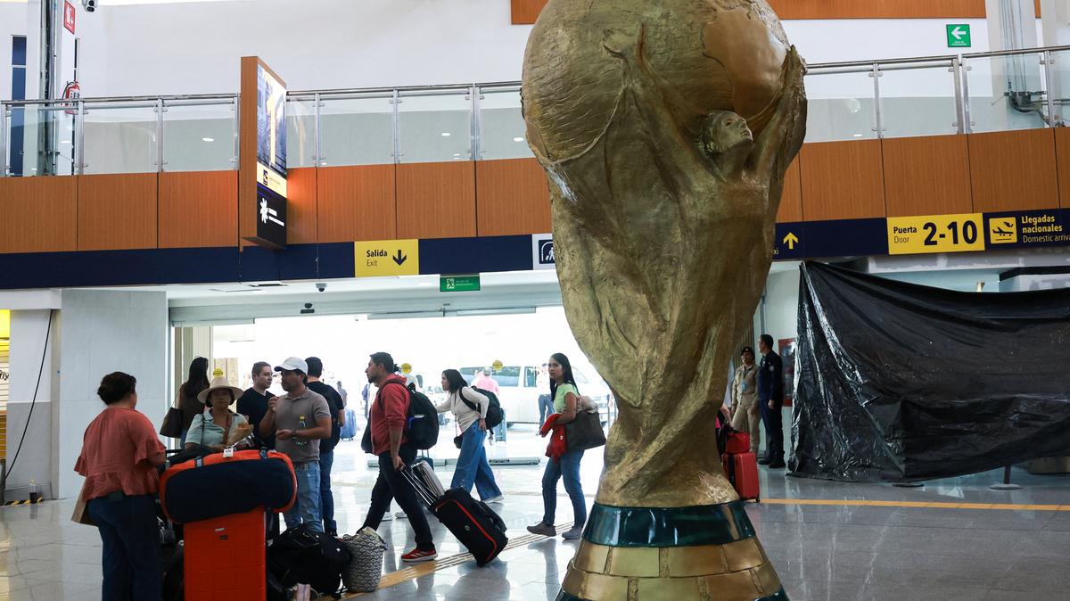 Passengers stand beside a giant replica of the World Cup trophy displayed at Mexico City International Airport, ahead of the World Cup starting on June 11, in Mexico City, Mexico, May 15, 2026. REUTERS/Henry Romero