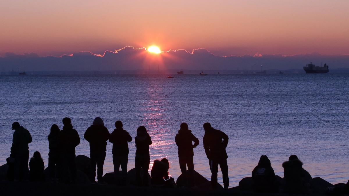 People watch the sun rise on New Year's Day at a beach along Tokyo Bay on January 1, 2016.    AFP PHOTO / Yoshikazu TSUNO (Photo by Yoshikazu TSUNO / AFP)