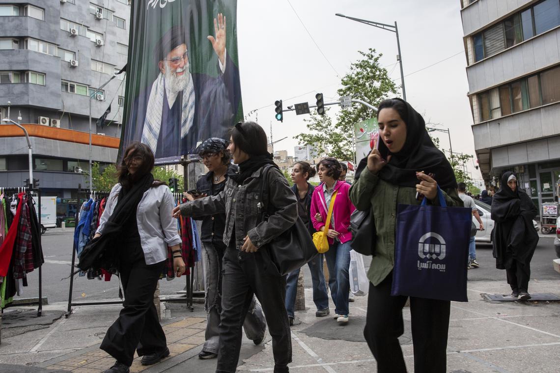 People walk under a banner of Ayatollah Ali Khamenei, Iran's slain supreme leader, in Tehran, on Monday, April 20, 2026. Despite sending mixed signals in recent days, both the United States and Iran gave clearer indications on Monday that they were planning to send negotiators to peace talks in Pakistan this week. (Arash Khamooshi/The New York Times)