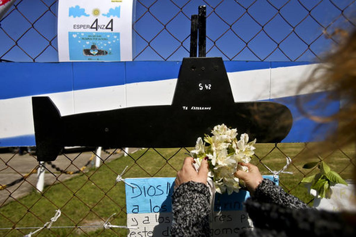 A woman places flowers by a cut out image of the ARA San Juan submarine on the fence at the naval base in Mar de Plata, Argentina, Friday, Nov. 24, 2017. The Argentine navy says an explosion occurred near the time and place where the submarine went missing on Nov. 15, leading some family members of the crew to give up hope of a rescue.