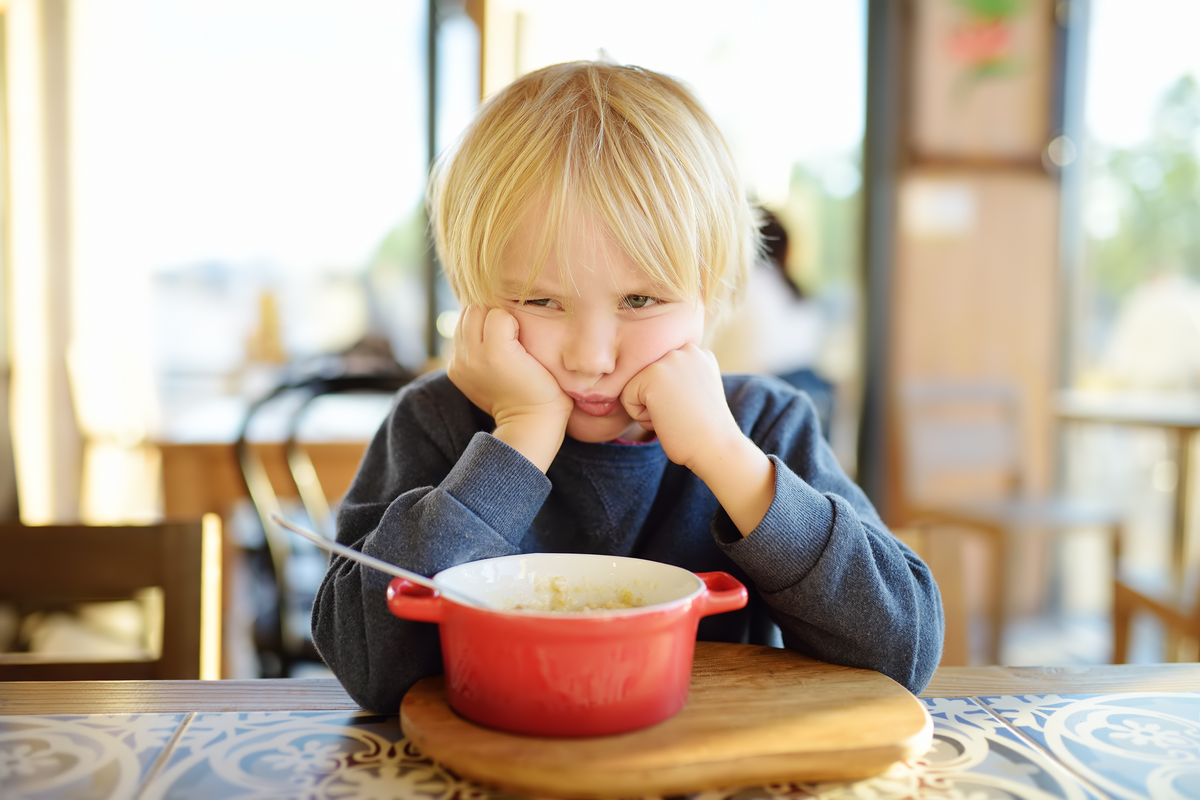  A stock photo of a young boy sitting at the table in cafe or restaurant and doesn’t want to eat. 