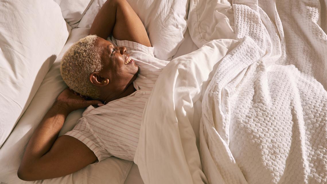 A mature woman wakes up and stretches in early morning light