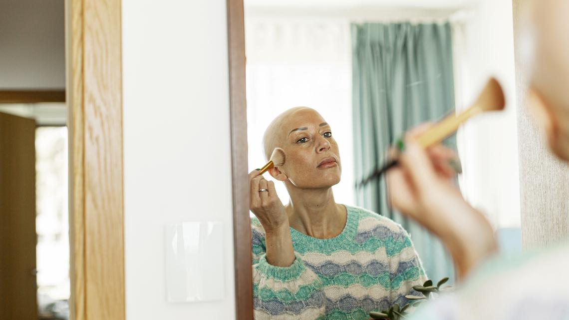 Reflection of woman with cancer applying blusher on cheek at home
