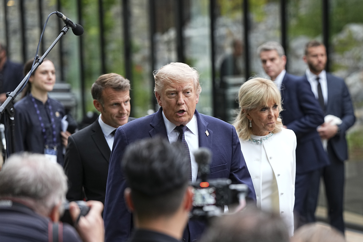 President Donald Trump speaks to reporters as he attends a cultural performance at the G7 Summit in Evian-les-Bains, France, June 16, 2026. President Emmanuel Macron of France, left, and Brigitte Macron walk behind him. (Haiyun Jiang/The New York Times)