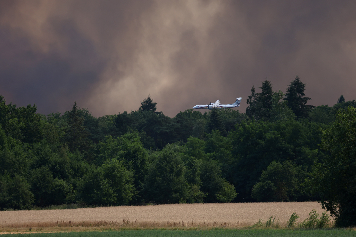 A Dash firefighting aircraft flies through plumes of smoke above the Fontainebleau forest as a wildfire burns near Paris during a heatwave affecting large parts of France, July 13, 2026. REUTERS/Stephane Mahe