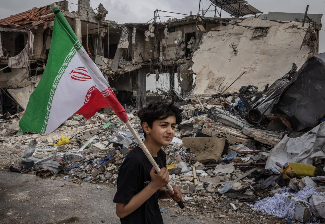Yusuf Mokaled, 14, carries an Iranian flag over his shoulder as he walks through the destruction in Tebnine, Lebanon, April 18, 2026. (David Guttenfelder/The New York Times)