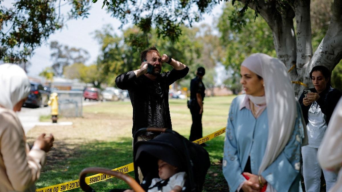 Members of the Muslim community use their phones at the scene of a reported active shooter situation at the Islamic Center, with yellow tape placed behind them to cordon the area, in San Diego, California, U.S., May 18, 2026.  REUTERS/Mike Blake