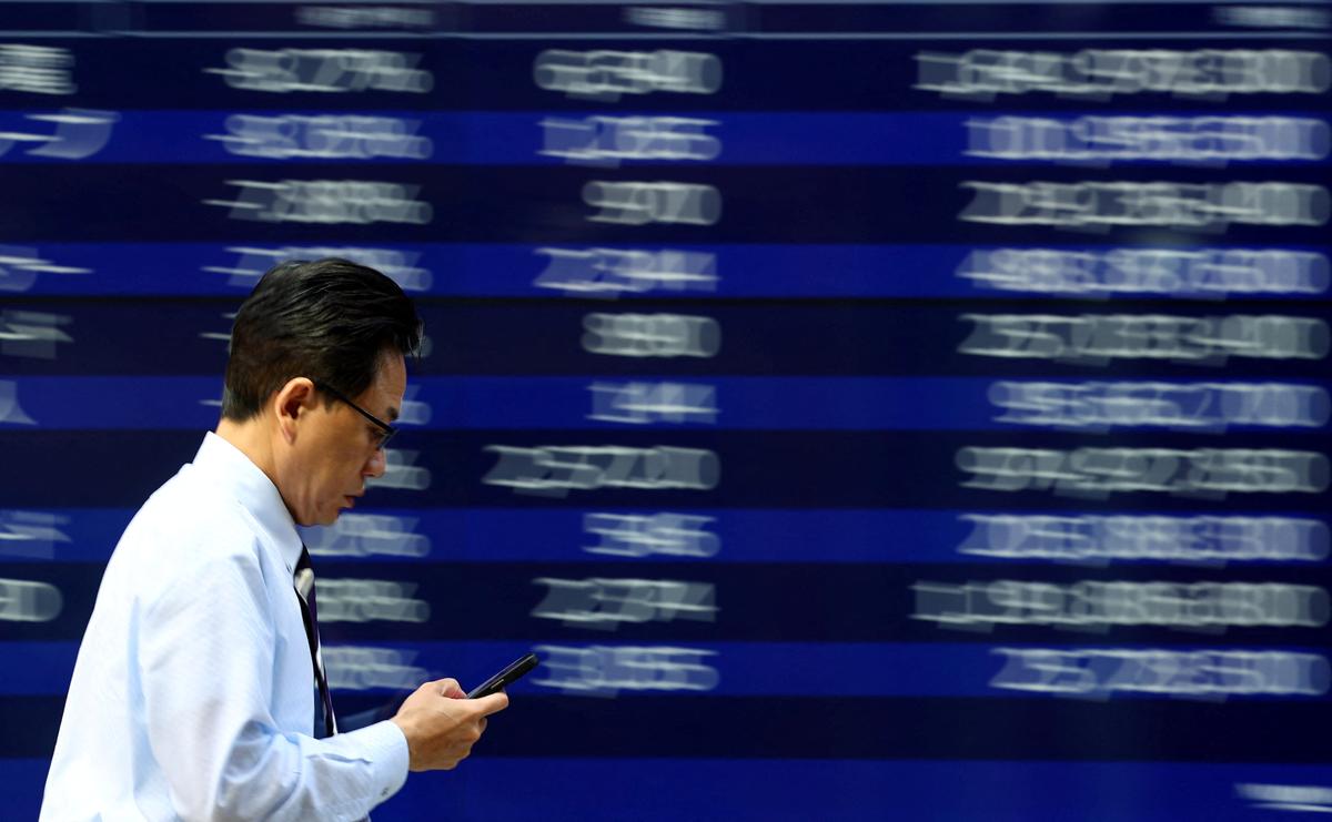 A man walks past an electronic screen displaying stock quotation board in Tokyo, Japan April 15, 2025. REUTERS/Issei Kato
