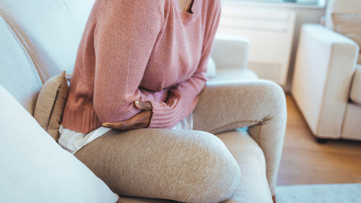 A stock image of a young woman lying down on her bed and suffering from period pains at home. 