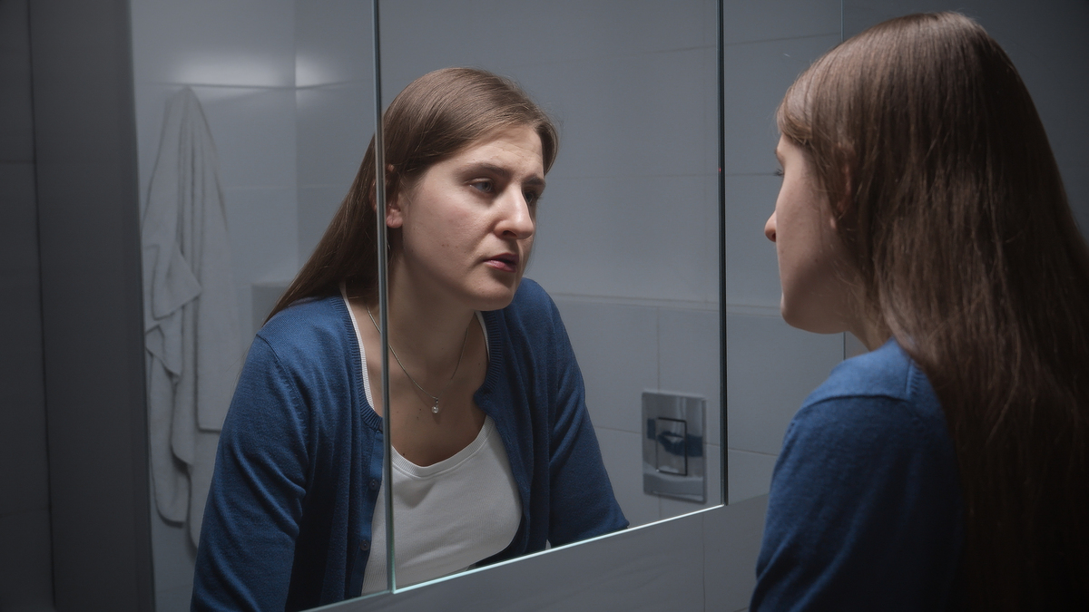  A stock image of an woman standing at sink and looking at her reflection. 