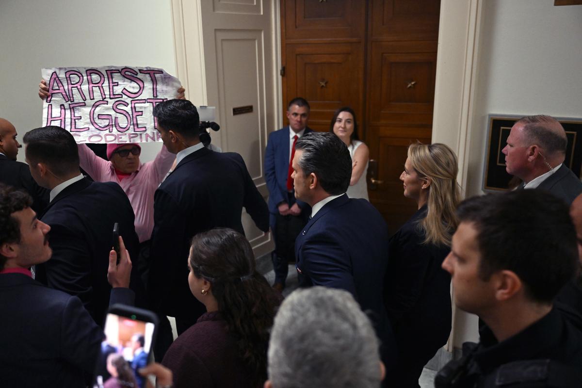 A protester holds up a sign as Defense Secretary Pete Hegseth, center, arrives at a hearing before the House Armed Services Committee in Washington on Wednesday morning, April 29, 2026. (Kenny Holston/The New York Times)