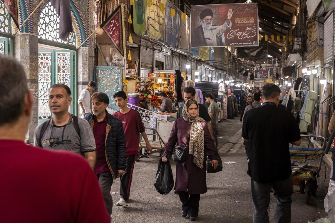 People walk at the Grand Bazaar under a banner of Ayatollah Ali Khamenei, Iran's slain supreme leader, in Tehran, on Monday, April 20, 2026. Despite sending mixed signals in recent days, both the United States and Iran gave clearer indications on Monday that they were planning to send negotiators to peace talks in Pakistan this week. (Arash Khamooshi/The New York Times)