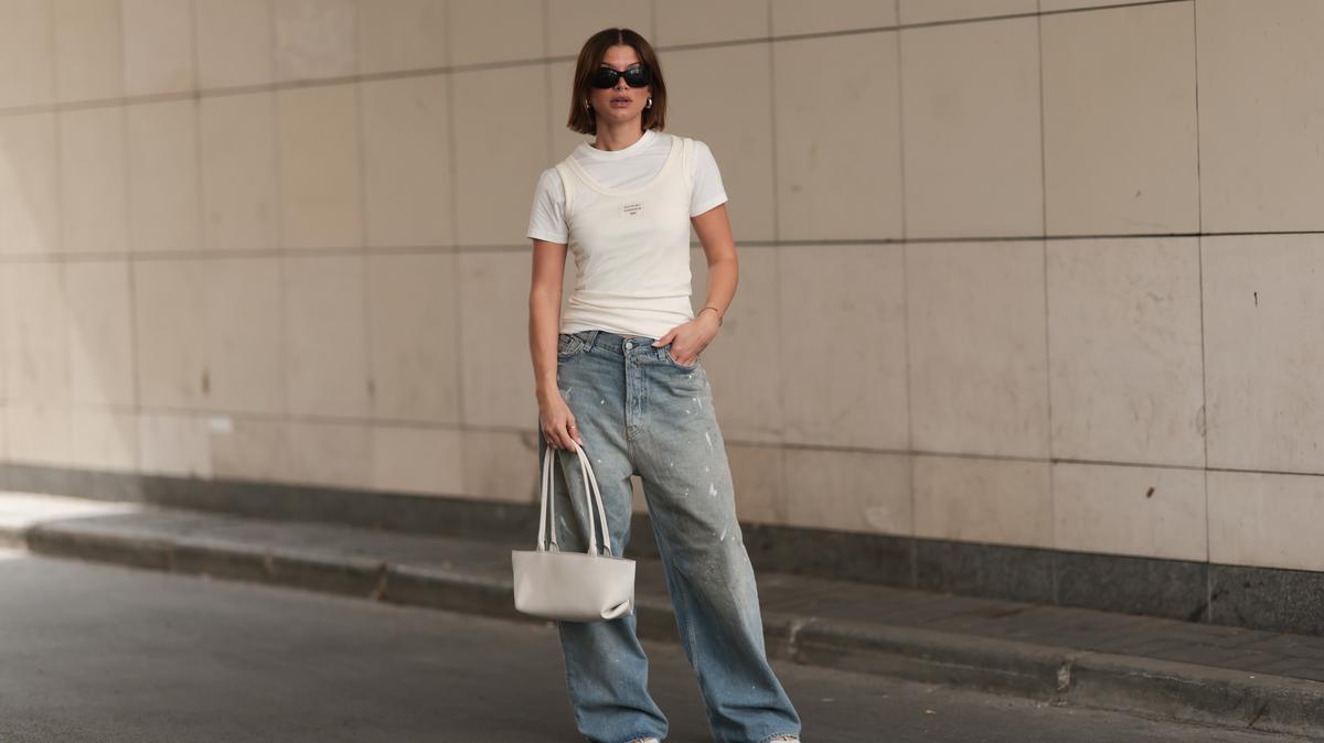 BERLIN, GERMANY - AUGUST 10: Sophia Geiss is seen wearing black round sunglasses, chunky silver hoop earrings, a silver nose ring, a white ribbed tank top from Acne Studios layered over a t-shirt, light blue wide-legged jeans with a baggy fit and black and white paint and smudge details also from Acne Studios, two minimalist silver rings, a gold bangle, a rectangular white leather bag with tubular shoulder straps from DeMellier, and pointed white leather pumps from Mango on August 10, 2025 in Berlin, Germany. (Photo by Jeremy Moeller/Getty Images)