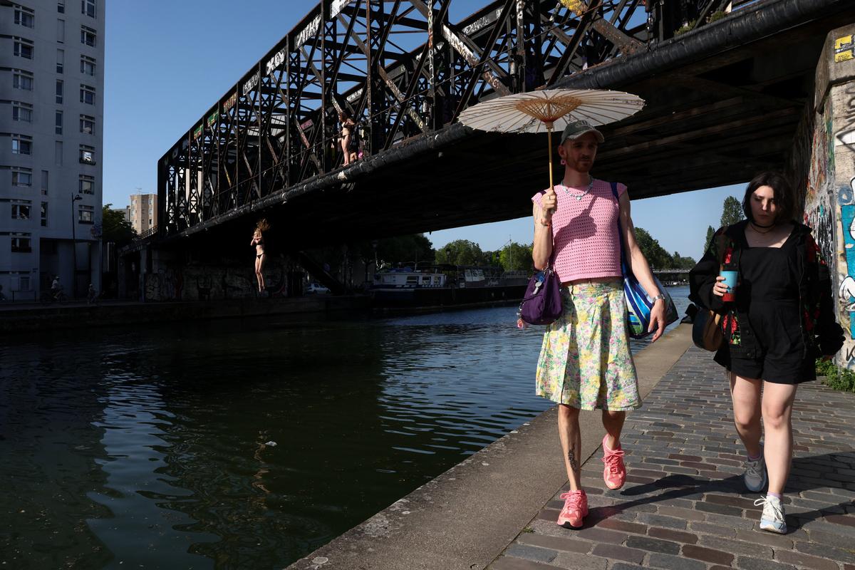 People walk along the Canal de l'Ourcq while another person jumps off a bridge into the canal, as temperatures reached up to 35 degrees Celsius, during a period of hot weather in Paris, France, May 25, 2026. REUTERS/Tom Nicholson