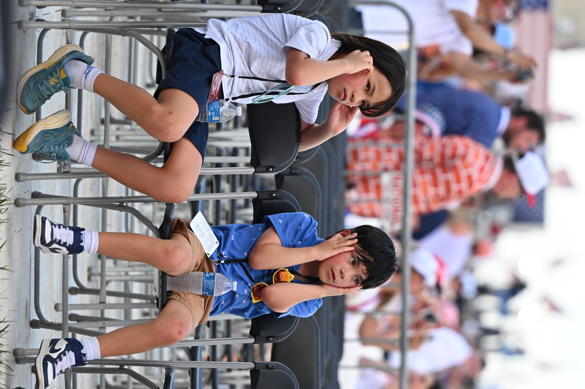 Children cover their ears as jets fly over the National Mall in Washington during the America 250 celebration on July 4, 2026. As an air show continued over the National Mall, the Washington Monument Grounds remained empty, with crowds for the "Salute to America" just starting to trickle in after the event was delayed due to heat. (Kenny Holston/The New York Times)