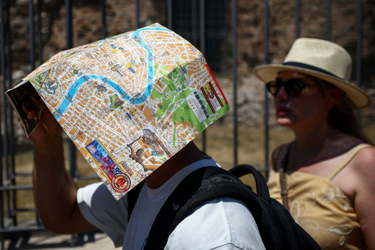 A tourist uses a map of Rome to shield their face from the sun beside the base of the Temple of Venus and Roma, opposite the Colosseum, during a heatwave in Rome, Italy, June 20, 2026. REUTERS/Guglielmo Mangiapane
