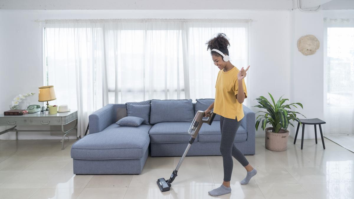 young woman with wireless headphones using vacuum cleaner for cleaning her house.