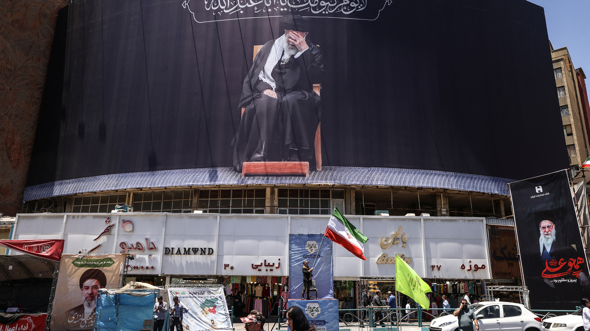 An Iranian woman waves a national flag under a billboard depicting slain supreme leader Ayatollah Ali Khamenei at Valiasr Square in Tehran on June 15, 2026. The United States and Iran agreed a peace deal and an "immediate and permanent" end to military operations on all fronts including Lebanon, mediator Pakistan said, signaling the apparent end to more than three months of war in Middle East. (Atta Kenare/AFP/Getty Images/TNS)