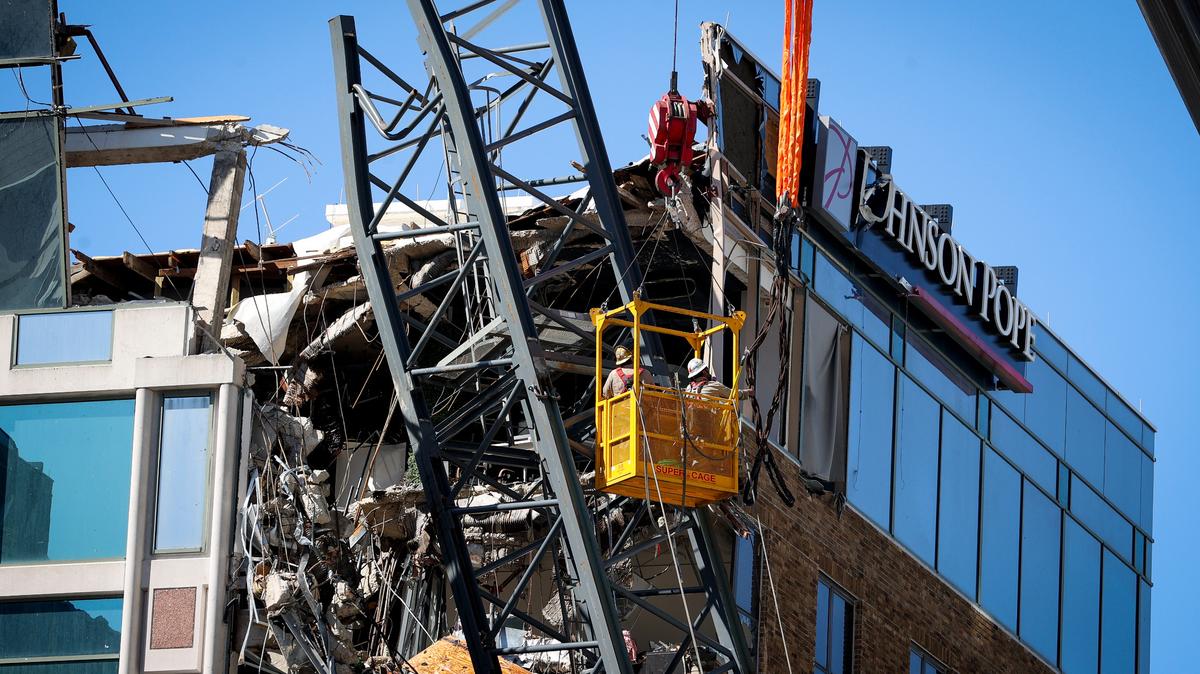 Workers are seen in a basket suspended near part of a crane that sits atop 490 First Ave. S. building Wednesday, Oct. 23, 2024 in St. Petersburg. The crane broke off and landed on the building during the high winds of Hurricane Milton.