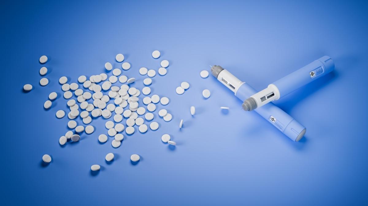 Weight loss pills available: Two dosing pens  for subcutaneous injection of antidiabetic medication or anti-obesity medication on a blue background besides a heap of GLP-1 pills.