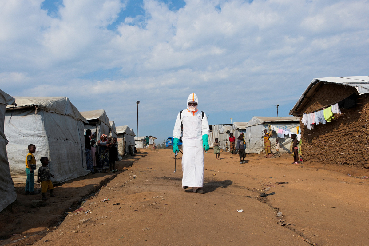 Displaced people watch a health worker in full personal protective equipment (PPE) preparing to disinfect the area during the burial of suspected Ebola victims at the Kigonze displaced persons camp in Bunia, eastern Democratic Republic of Congo, on June 18, 2026, one month after the outbreak was declared. REUTERS/Gradel Muyisa Mumbere