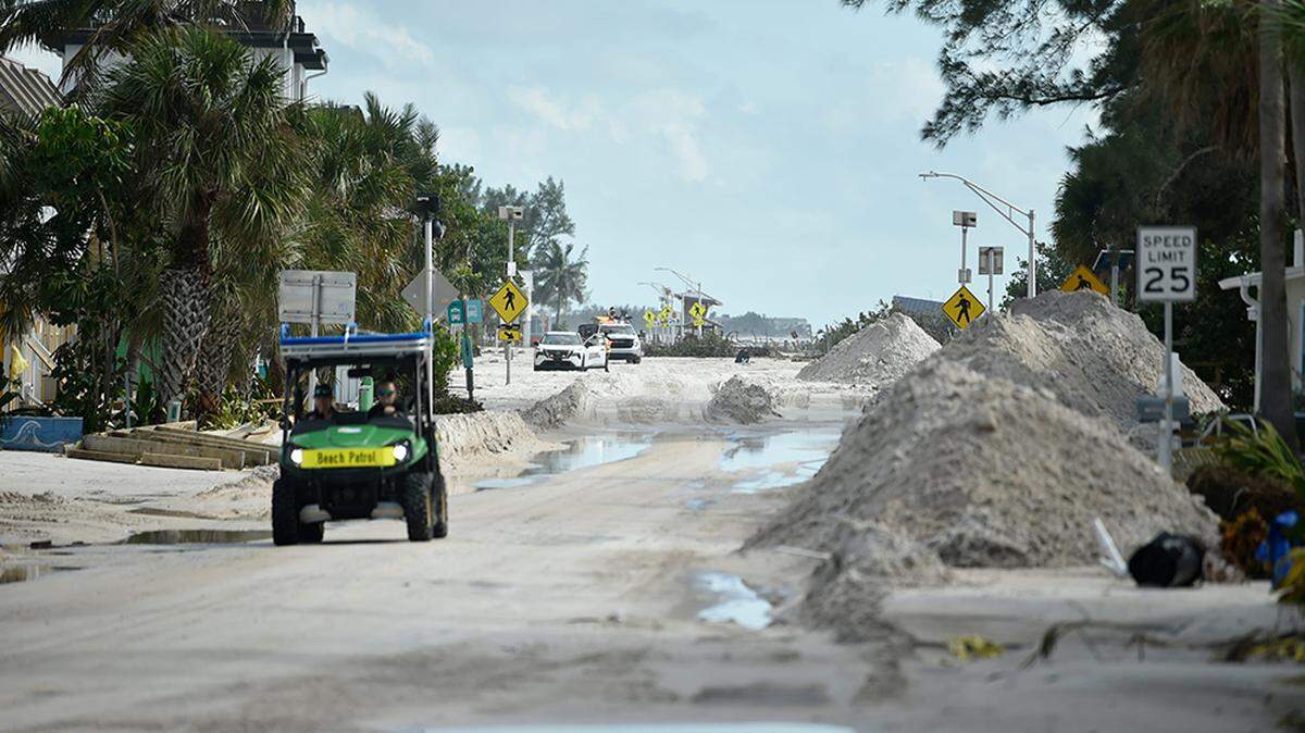 Trabajadores retiran arena de la carretera en Bradenton Beach, en la isla Anna Marie, Florida, mientras los grandes camiones retiran los escombros.