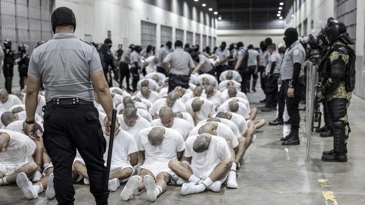 In this photo provided by El Salvador’s presidential press office, a prison guard transfers deportees from the U.S., alleged to be Venezuelan gang members, to the Terrorism Confinement Center in Tecoluca, El Salvador, Sunday, March 16, 2025.