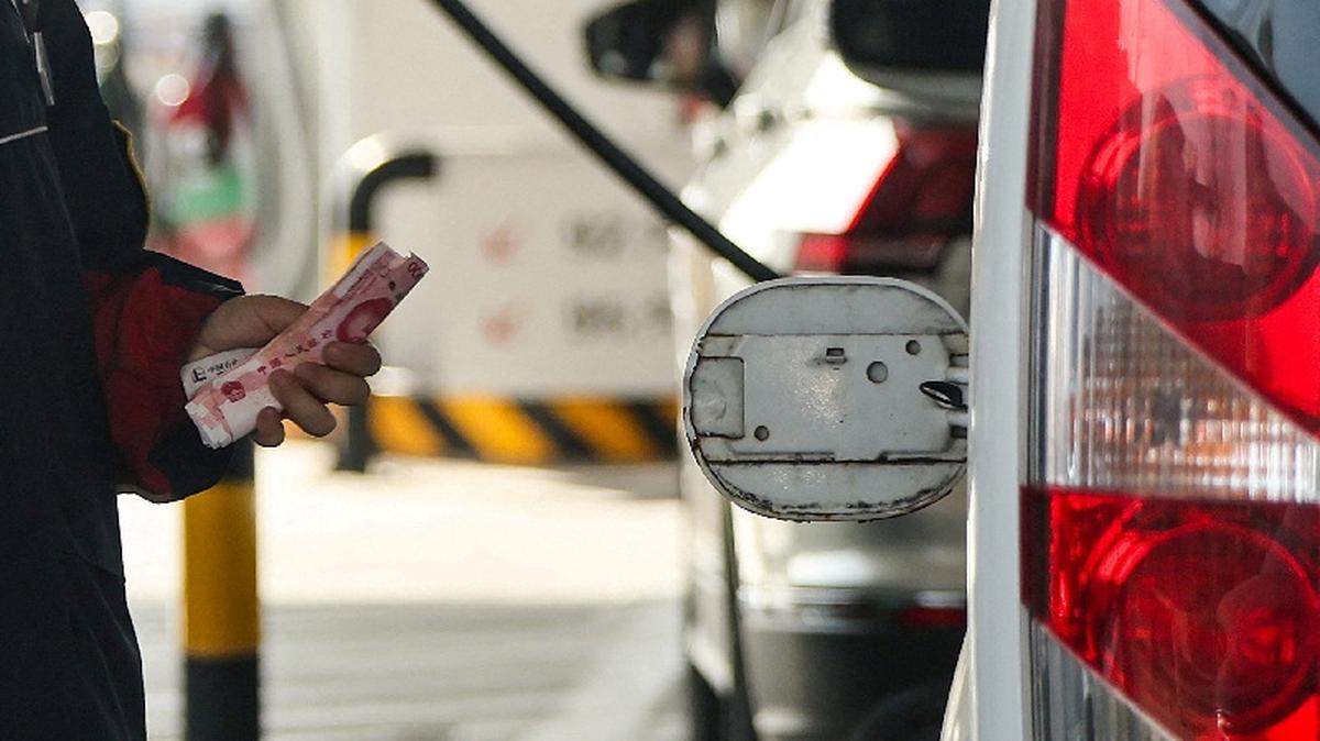 FILE PHOTO: An employee holds Chinese Yuan notes next to an open cap of a car's fuel tank at a gas station ahead of an announced fuel price hike, amid the U.S.-Israeli conflict with Iran, in Beijing, China, March 22, 2026. REUTERS/Maxim Shemetov/File Photo