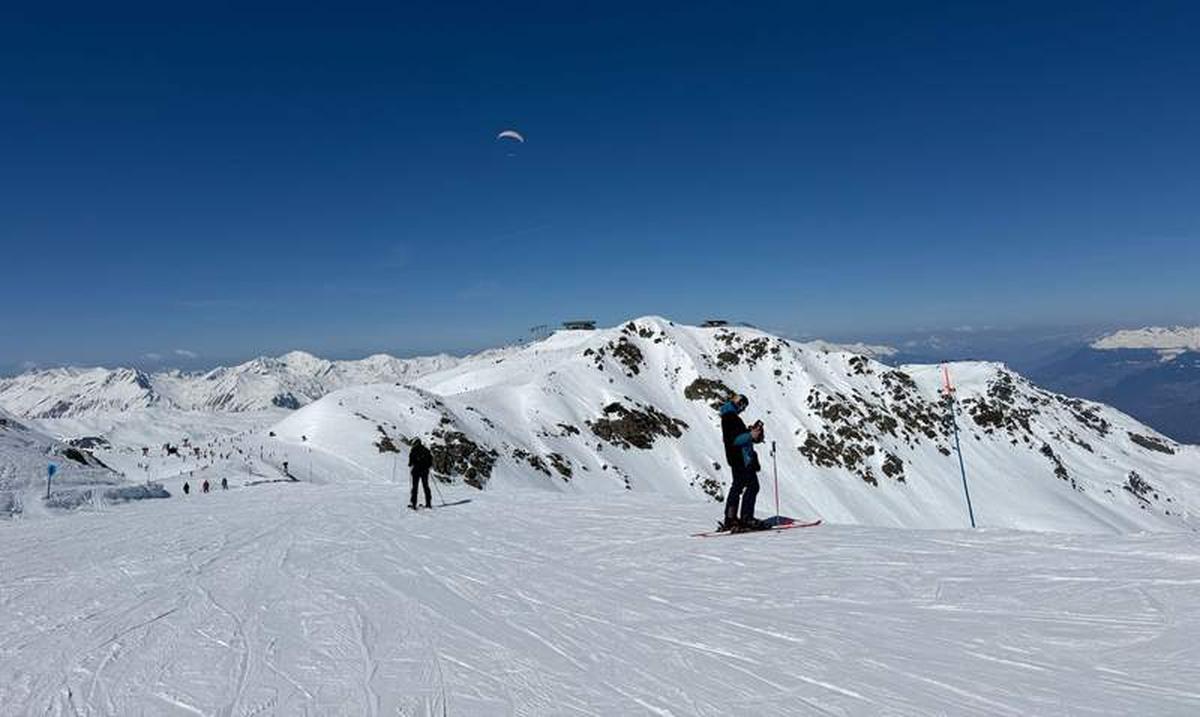  Above Val Thorens near Caron 3200, a paraglider drifts overhead while skiers take a moment to soak in the kind of view that makes you forget you were about to push off. Photo credit: Liana Moore 