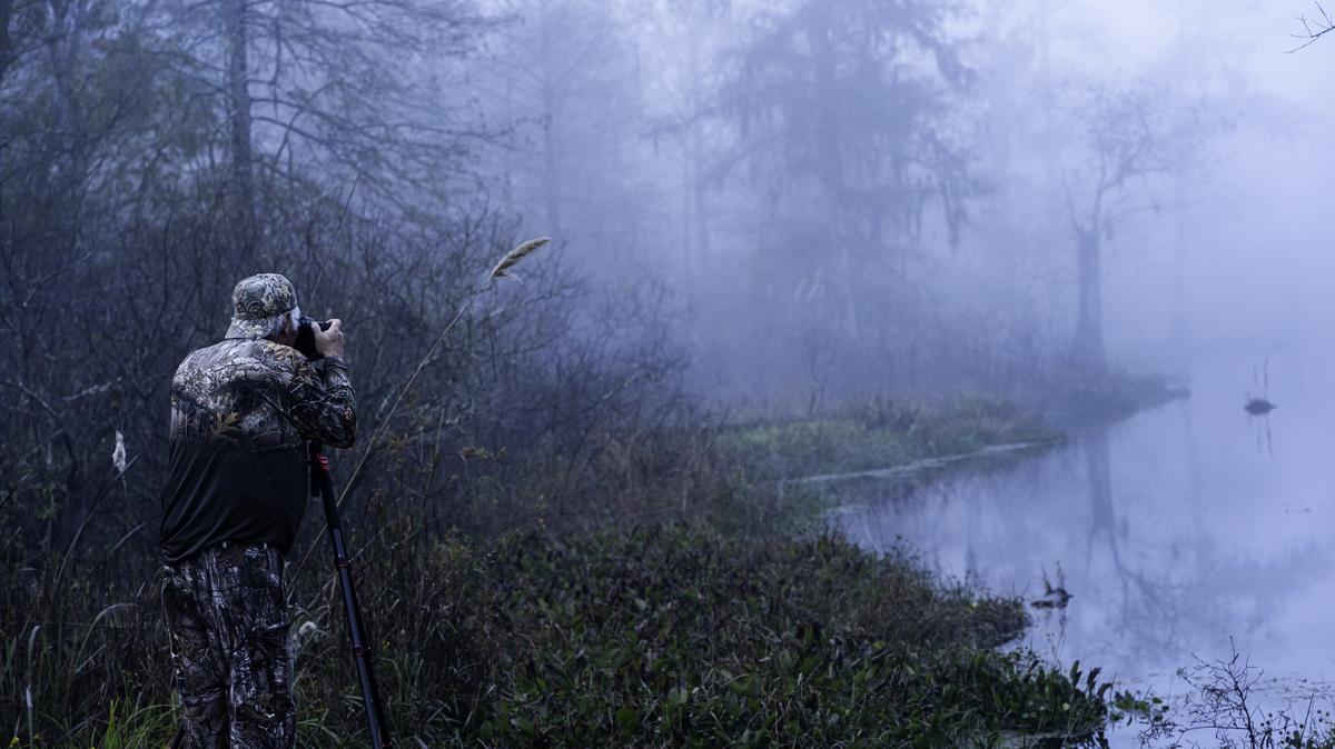 Photographing a misty morning at Lake Martin. Breaux Bridge, Louisana, USA - November 21, 2020: A man uses a tripod to photograph a misty morning from the edge of Lake Martin on opening day of duck hunting.