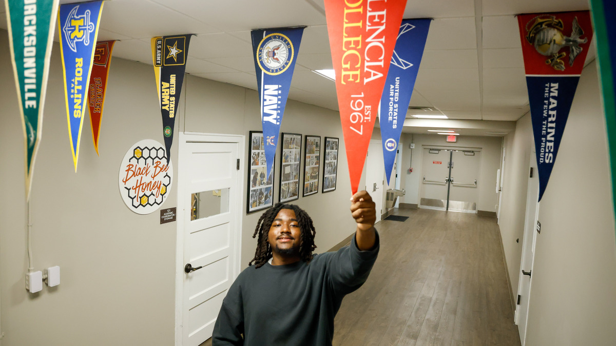 Seon Victor grabs hold of a Valencia College pennant that hangs in the hallway at Parramore Kidz Zone in Orlando, Fla., on June 1, 2026. Victor, now a student at Valencia College and an aspiring author, grew up utilizing the community center’s after-school activities that helped instill his love for writing.